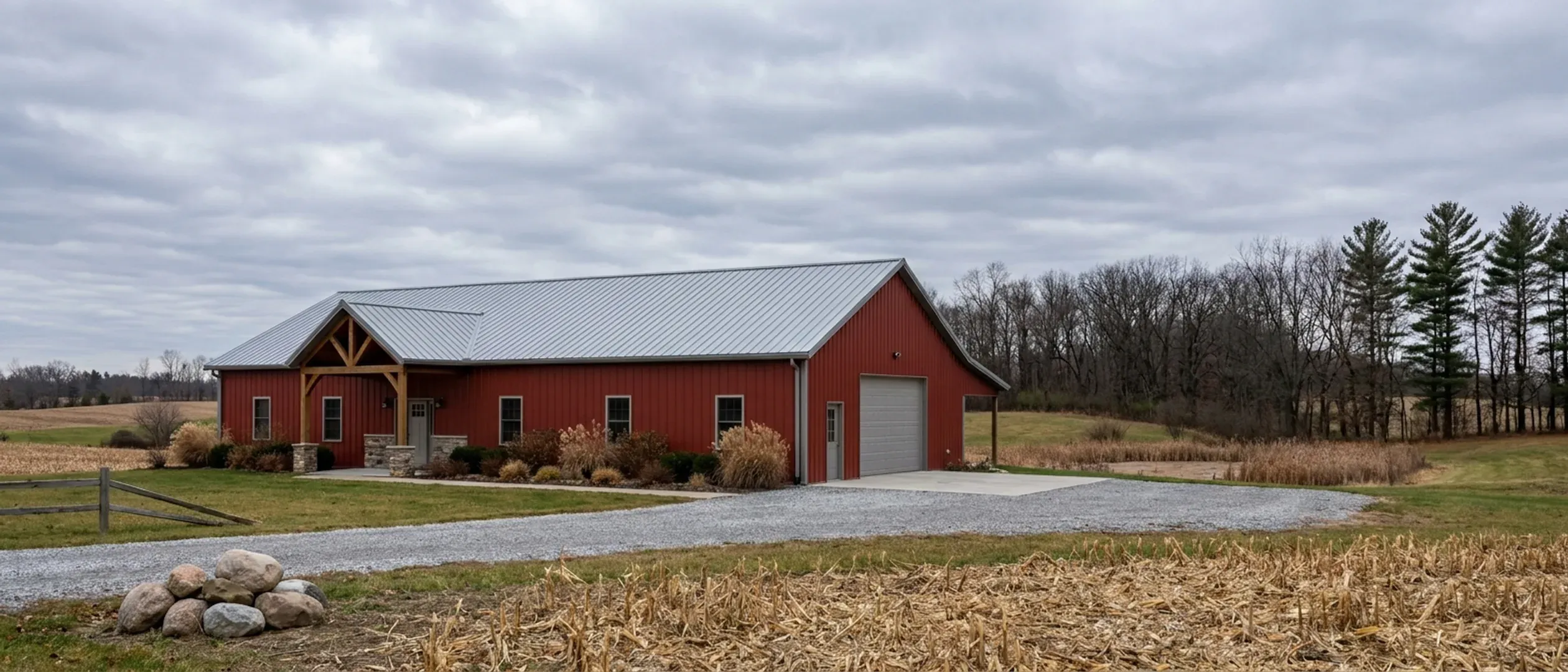 A completed barndominium with a covered entry porch and an attached shop bay, photographed in flat overcast late-autumn daylight. A completed barndominium with a covered entry porch and an attached shop bay, photographed in flat overcast late-autumn daylight.